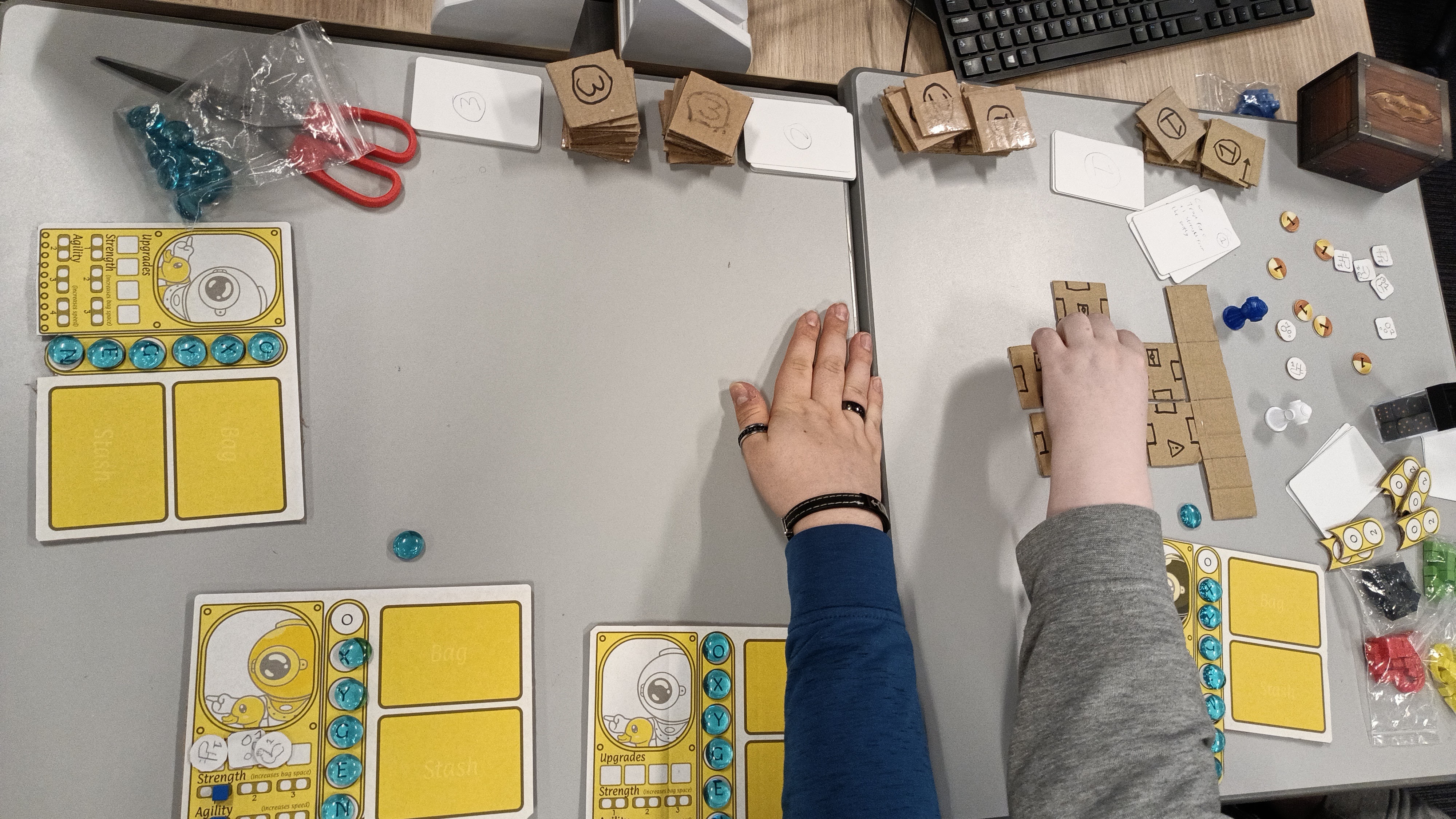 3 people playing handmade board game with cardboard tiles and divers